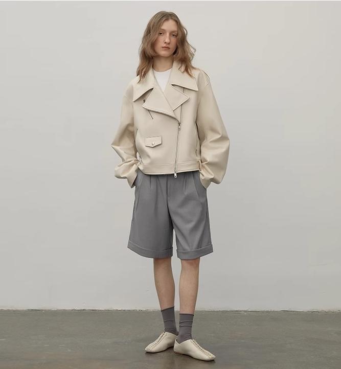 Person wearing a beige jacket and gray shorts against a plain background