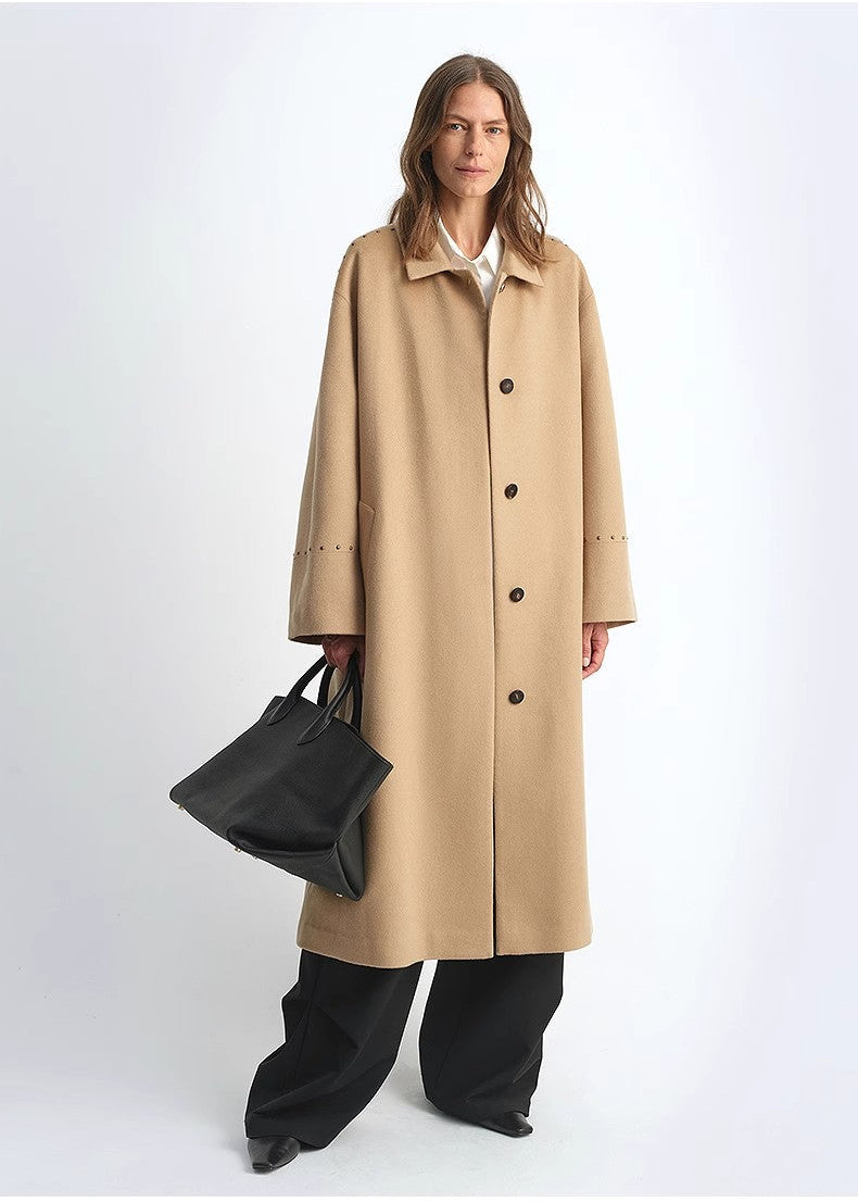 Woman wearing a beige trench coat holding a black handbag on a white background