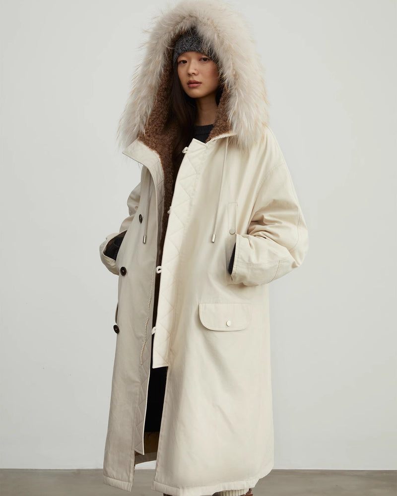 Person wearing a long cream coat with a fur-lined hood against a plain background