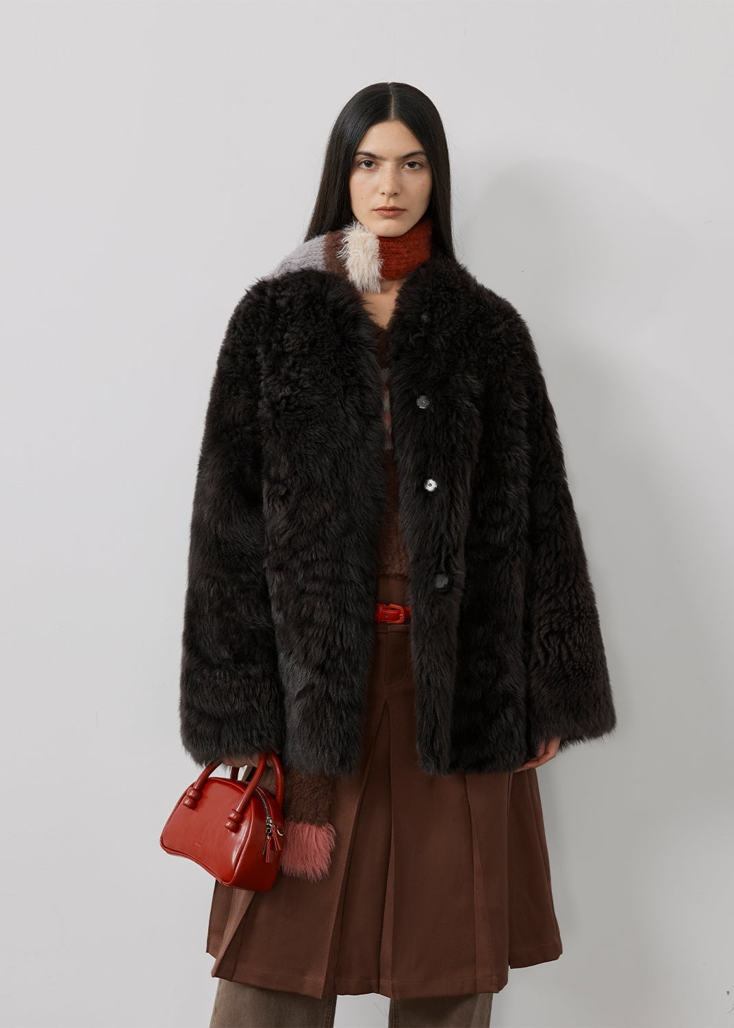 Woman wearing a black fur coat with a red handbag on a white background
