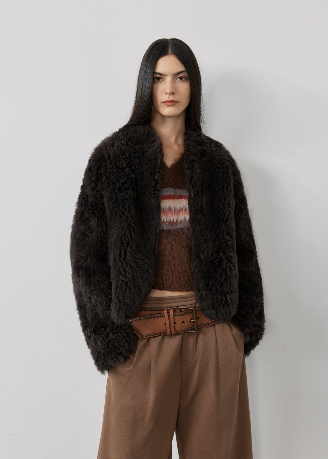 Woman wearing a dark brown fur coat over a patterned sweater with a plain background